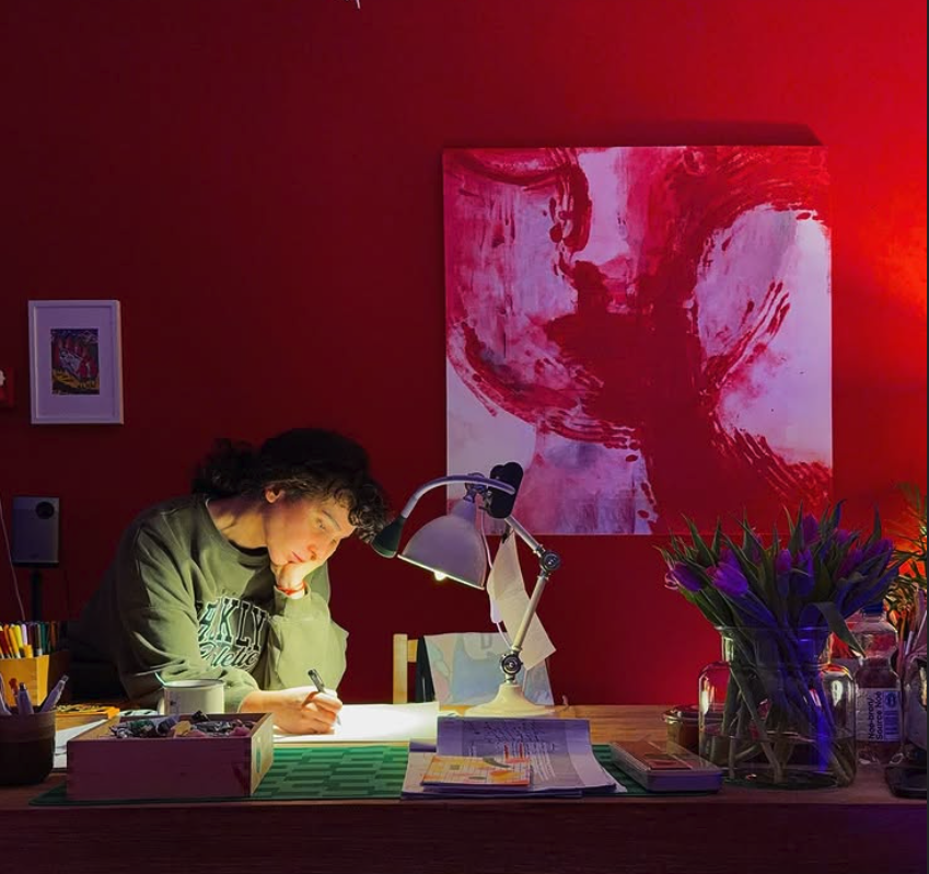 Shaqayeq drawing in her red-lit studio